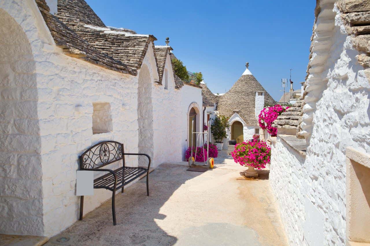 A street lined with white buildings with thatched roofs called 'trulli' under a clear blue sky.