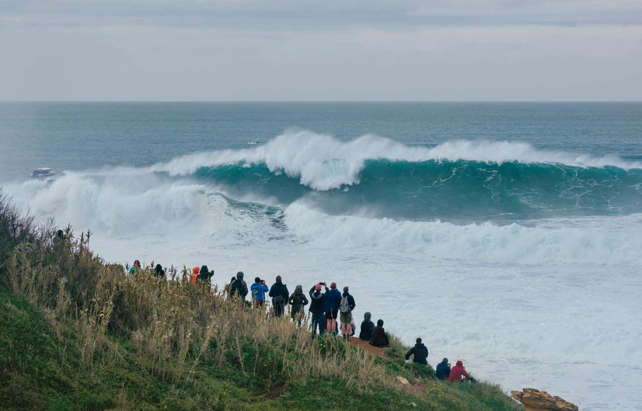 Une vague géante à Nazaré, lieu réputé dans le monde entier pour le surf ; personne admirant les vagues