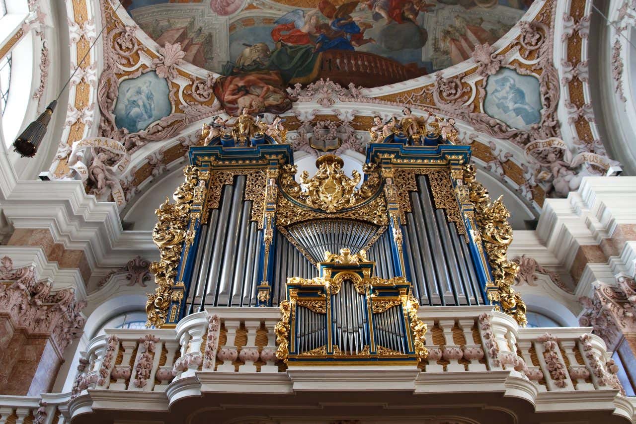 Organo a canne barocco ornato d'oro e blu all'interno di una chiesa decorata con affreschi e stucchi elaborati