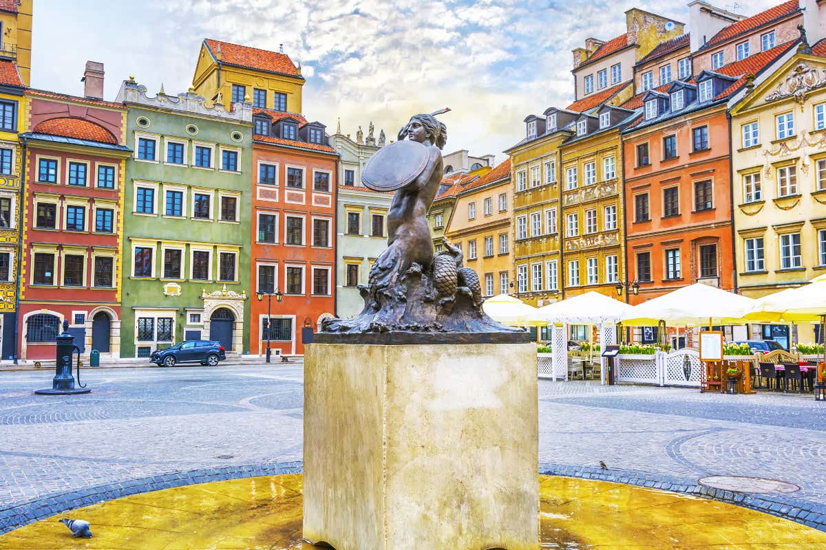 Escultura de una sirena en el centro de una plaza con casas y edificios de colores