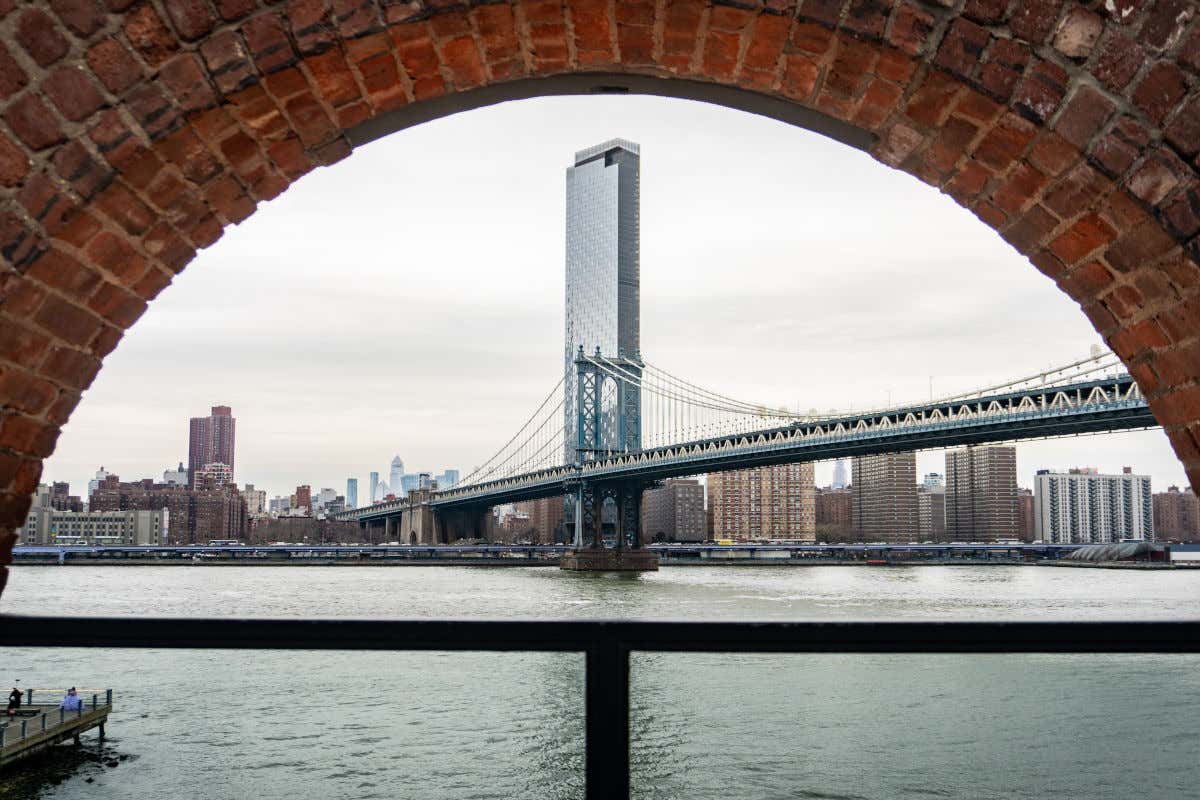 Un arco de ladrillo a través del cual se puede ver el mar y el puente de Manhattan