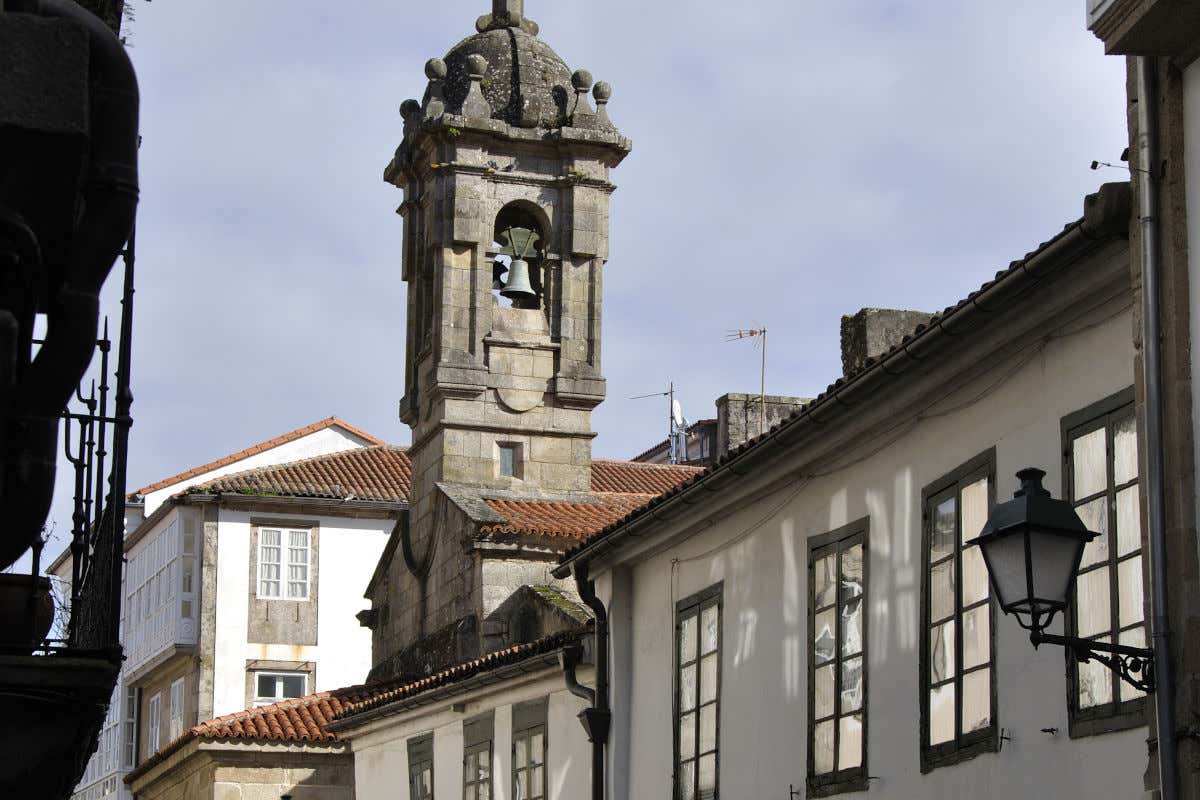 Una torre de una pequeña iglesia de piedra en mitad de una calle de Santiago de Compostela en un día despejado