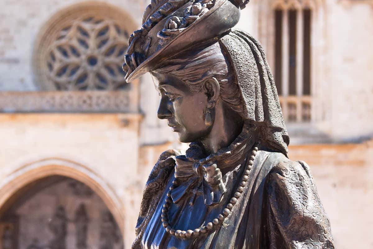 Escultura de una mujer con vestimenta de época frente a una catedral