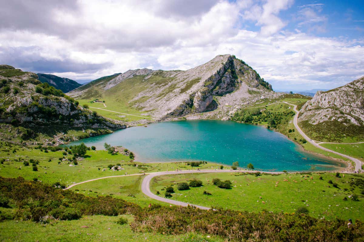 Panorámica de uno de los lagos de Covadonga con unas aguas azul turquesa rodeadas de montañas y verdes prados en un día nublado