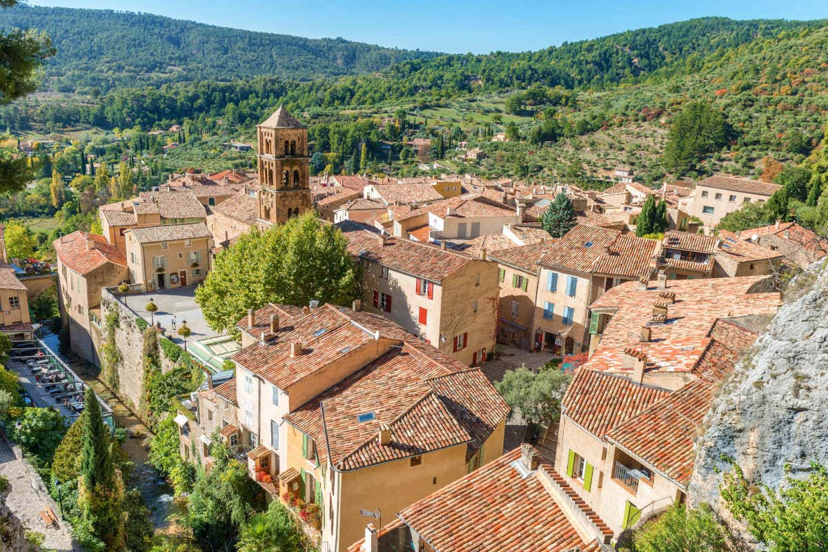 Pueblo medieval rodeado de una frondosa vegetación, con el campanario de una iglesia en primer término