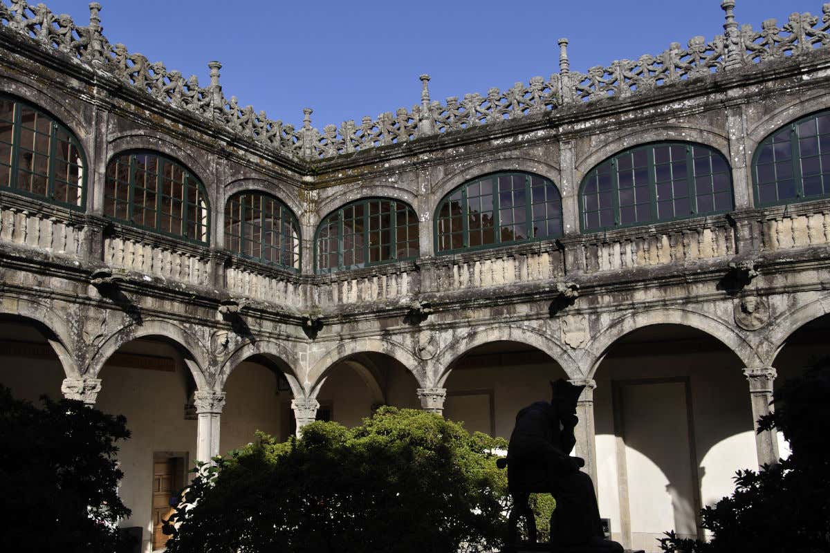 Un patio interior de un edificio histórico con varias galerías arqueadas, árboles y una escultura de un hombre pensando