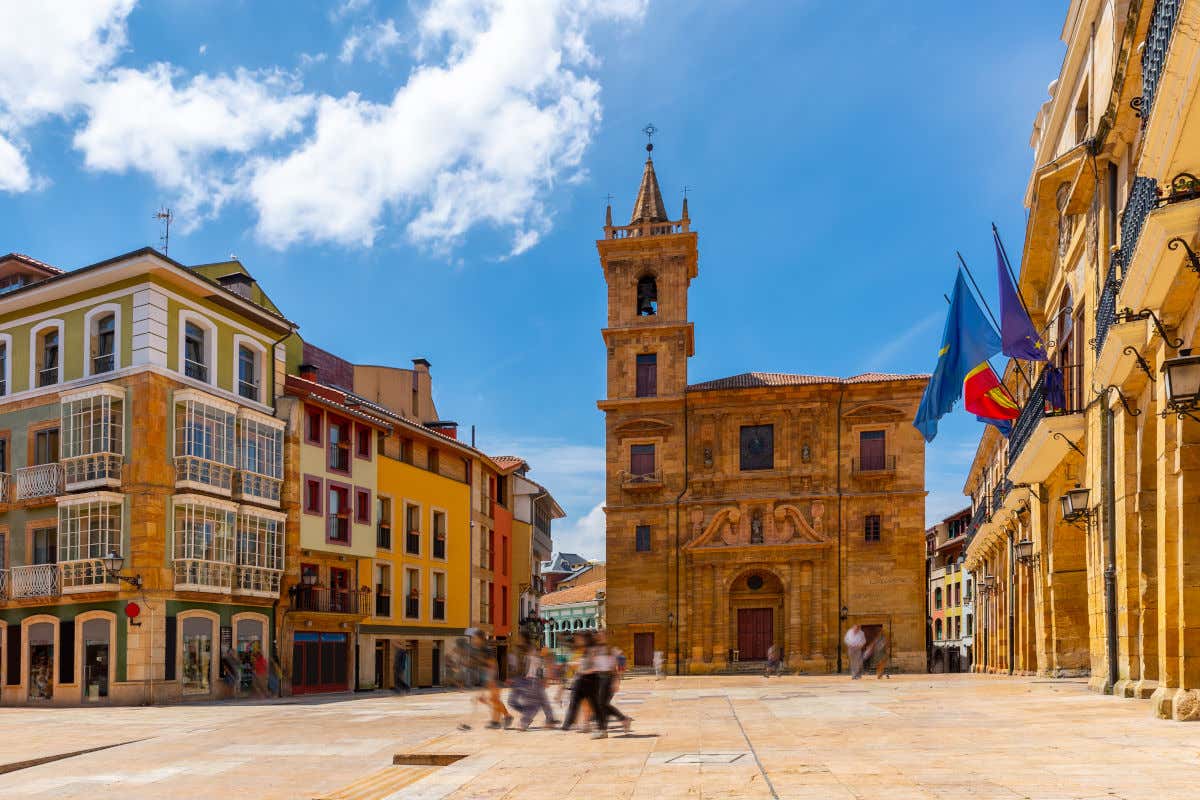 Una plaza flanqueada por una iglesia, varias casas de colores y la fachada de un ayuntamiento decorado con banderas
