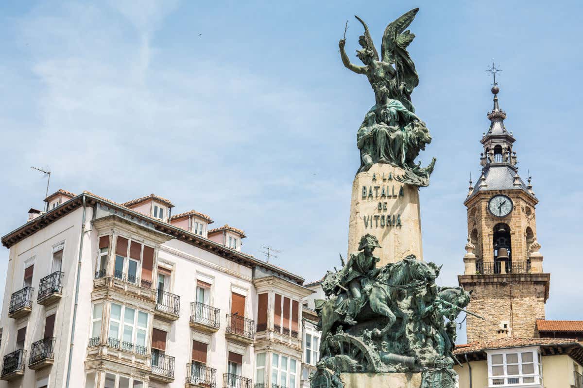 Un obelisco decorado con numerosas esculturas frente a la torre del reloj de una iglesia