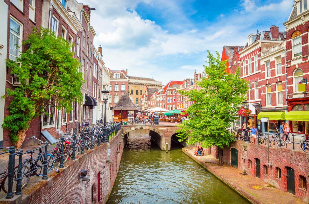 Landscape view looking down a canal in Utrecht, one of the best cities for biking, bikes chained to the railing on the leftside of the canal, bikers riding on the right