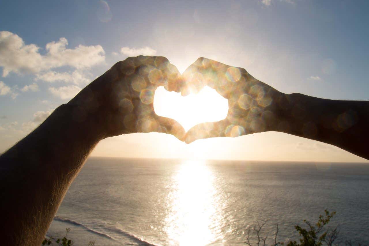 Mãos fazendo um formato de coração no pôr do sol do fortinho do Boldró