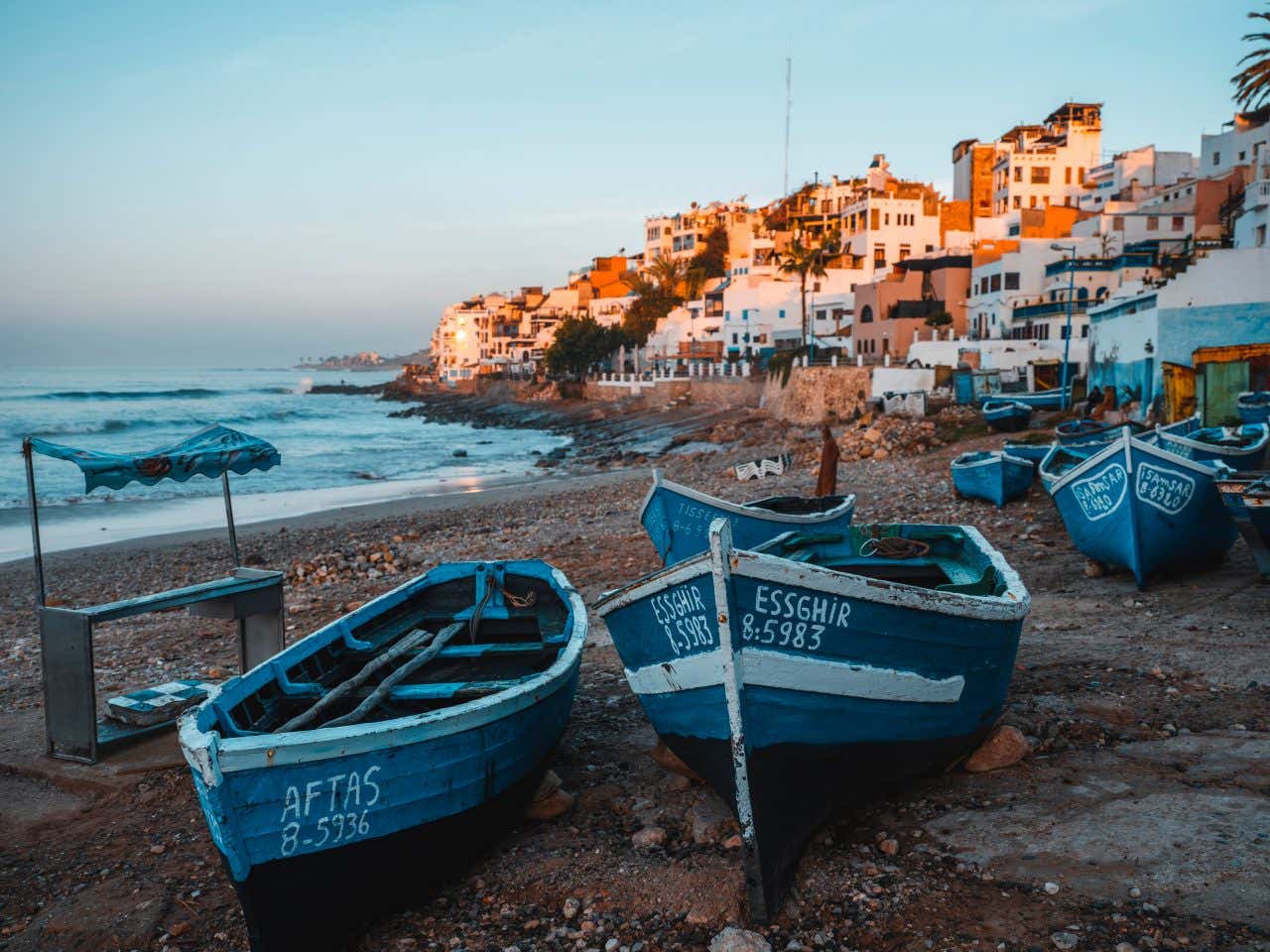 Lever de soleil sur la plage de Taghazout avec le village en arrière-plan et des barques de pêche au premier plan