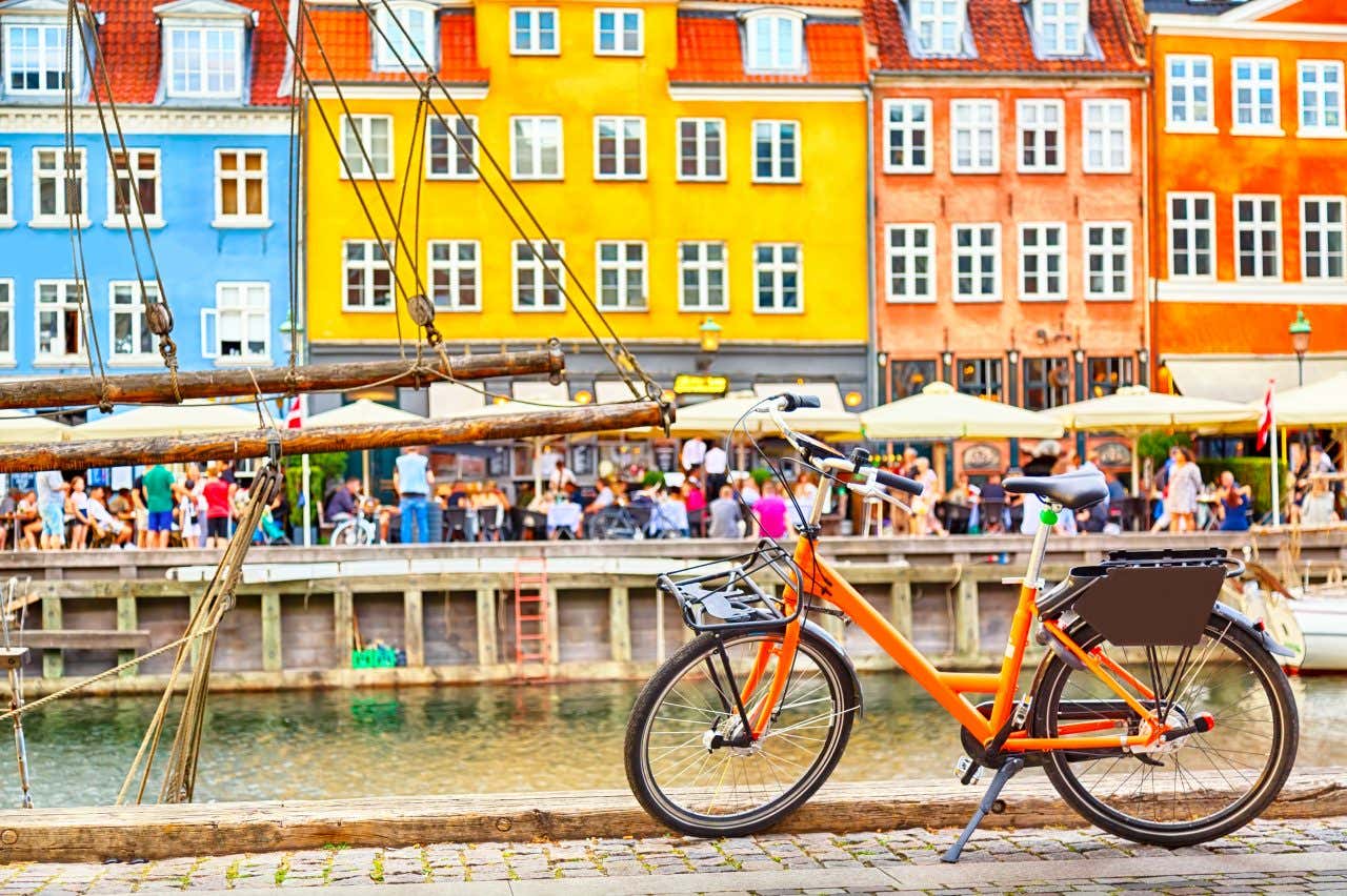 An organe bike parked on the opposite side of the Nyhavn Canal in Copenhagen, restaurants and people enjoying the outdoor terraces