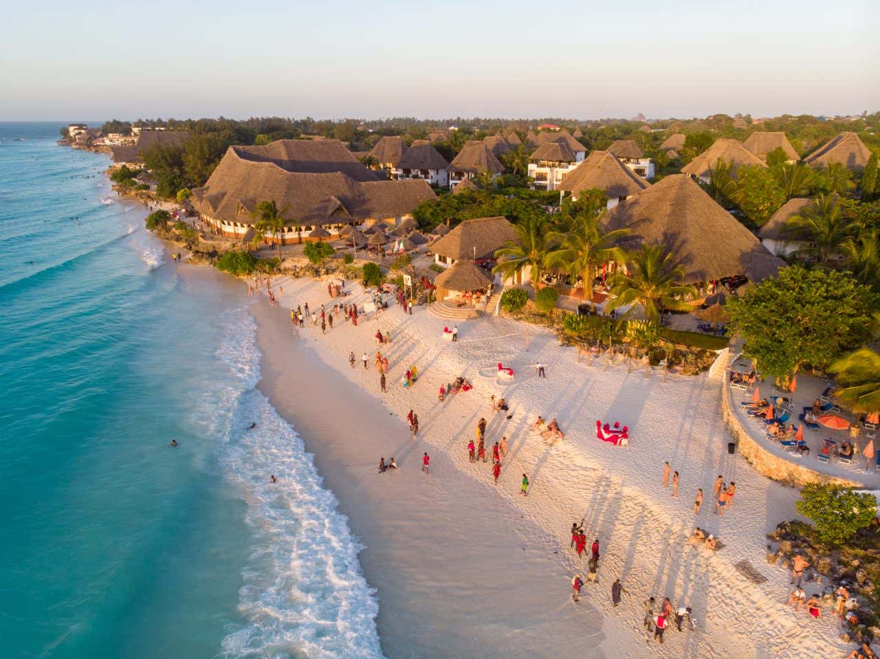 Vue aérienne sur la plage et village de Nungwi en fin de journée, avec des personnes se promenant sur le sable