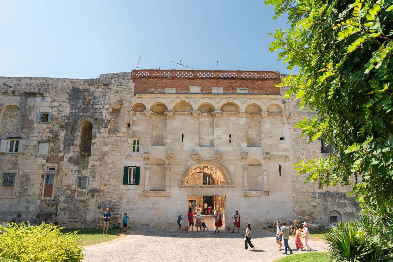 The Golden Gate (Porta Aurea) of Diocletian's Palace in Split, Croatia, a large stone archway forming an entrance to the ancient complex. People are walking through the arch, and the stone walls have various architectural details.
