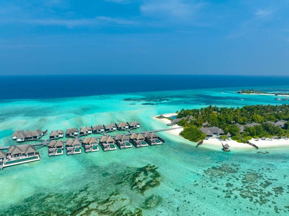 Vista aerea di un atollo delle Maldive con bungalow sull'acqua circondati da lagune turchesi e vegetazione tropicale