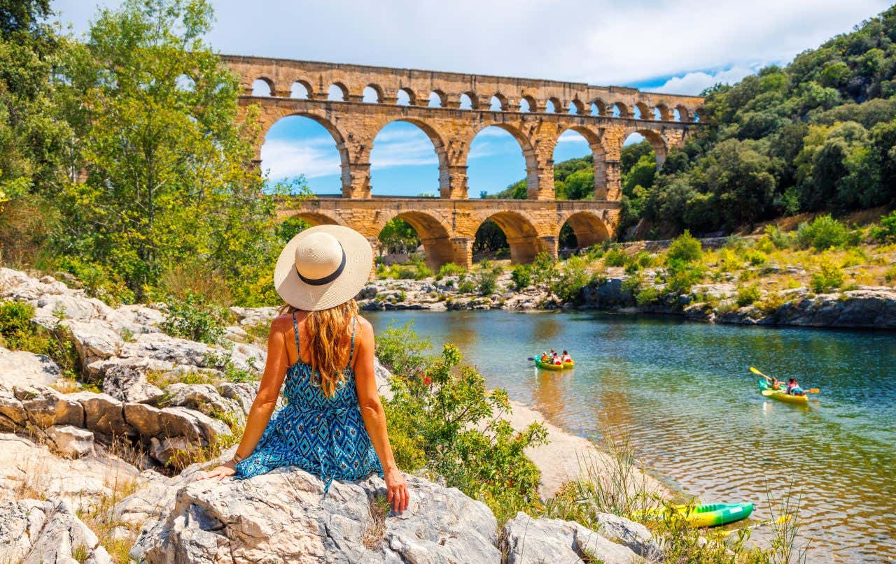 Jeune femme de dos avec un chapeau face au Pont du Gard et des kayakistes sur l'eau