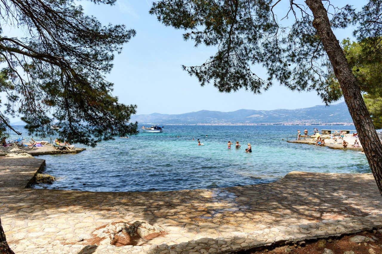 A shot of Bene Beach, Croatia, with people swimming in the water, and a mountain skyline in the background.