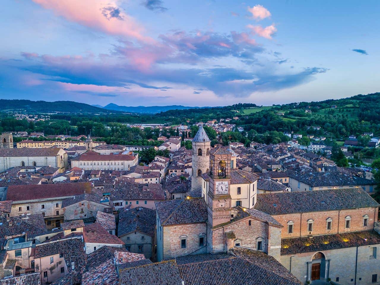 Vista aerea di Città di Castello, con i tetti a spiovente in tegole marroni e il campanario della basilica in primo piano. Le luci appena accese suggeriscono che la foto è stata scattata al tramonto