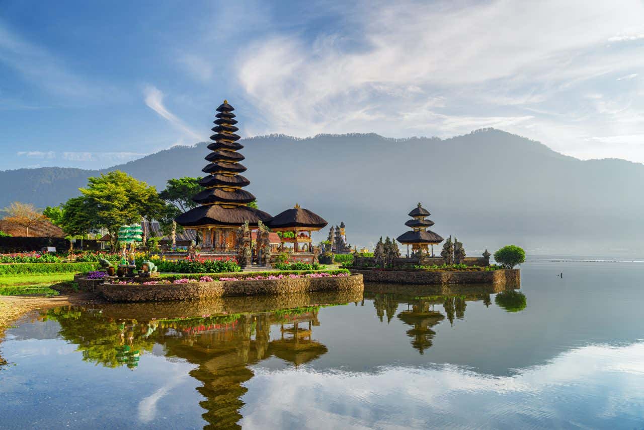 Un tempio a forma di pagoda costruito proprio sul limitare dell'acqua. Alle sue spalle si intravede il profilo di un monte, entrambi si riflettono sullo specchio del mare calmo e placido dell'isola di Bali, in Indonesia