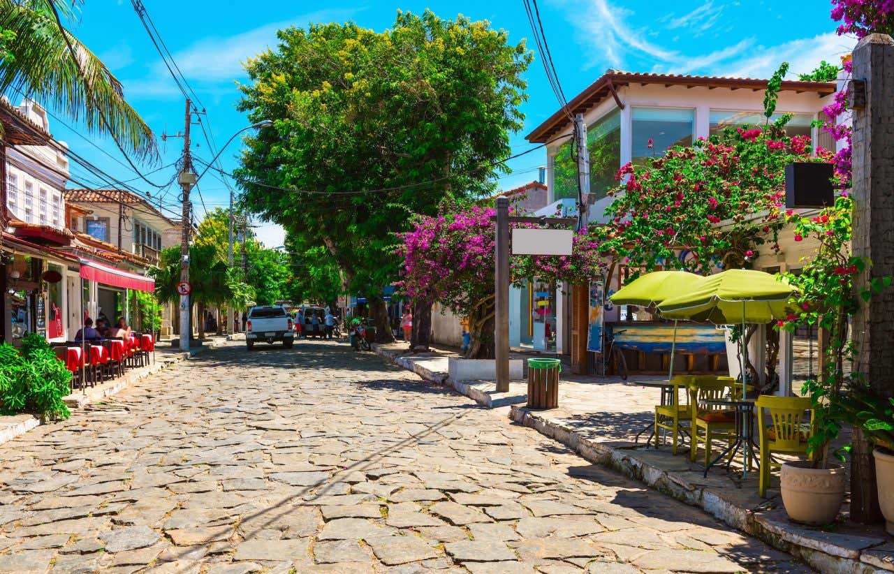 Visual rústico da Rua das Pedras em Búzios, com casas, restaurantes e mesas nas calçadas e rua de paralelepípedos