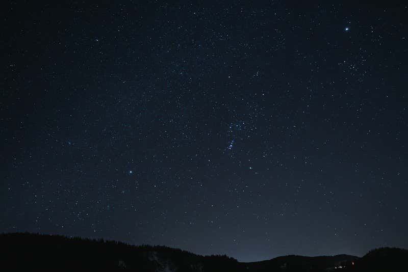 Panorámica del cielo estrellado nocturno con unas montañas de fondo, uno de los mejores sitios para ver estrellas en España