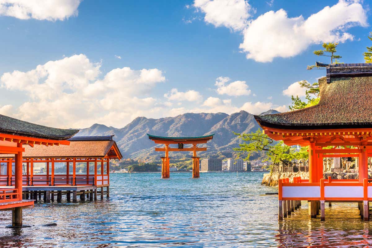 Un conjunto de templos japoneses de color rojizo en mitad del mar y frente a unas montañas