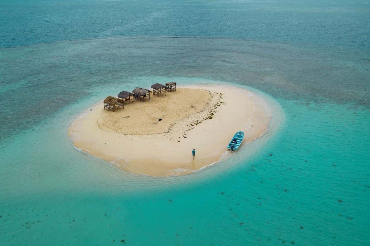 Un cayo de arena blanca con unas sombrillas de pajas en medio del mar en vista aérea