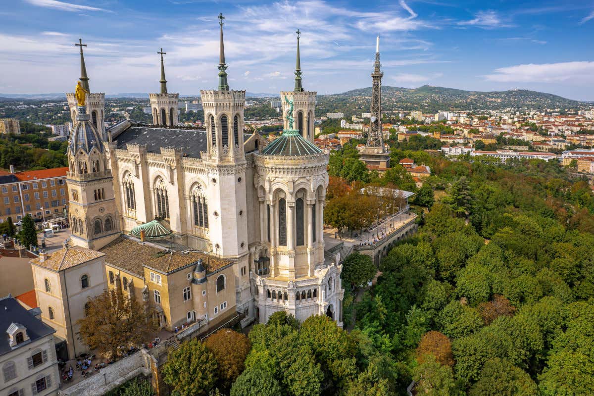 La basílica de Notre-Dame de Fourvière con diversas torres se alza en la cima de un monte rodeada de árboles y con vistas panorámicas a las casas de Lyon
