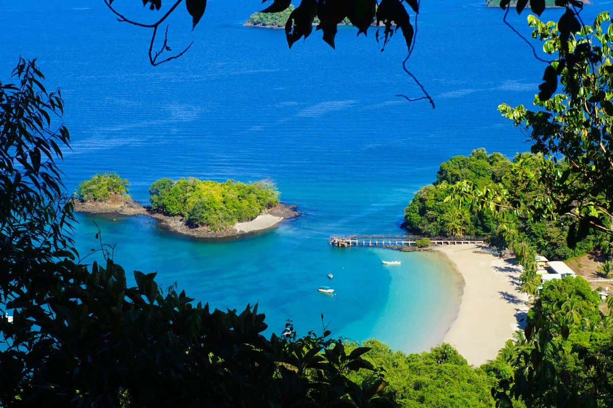 Vista de una playa de arena blanca frente a una isla desde un mirador con árboles