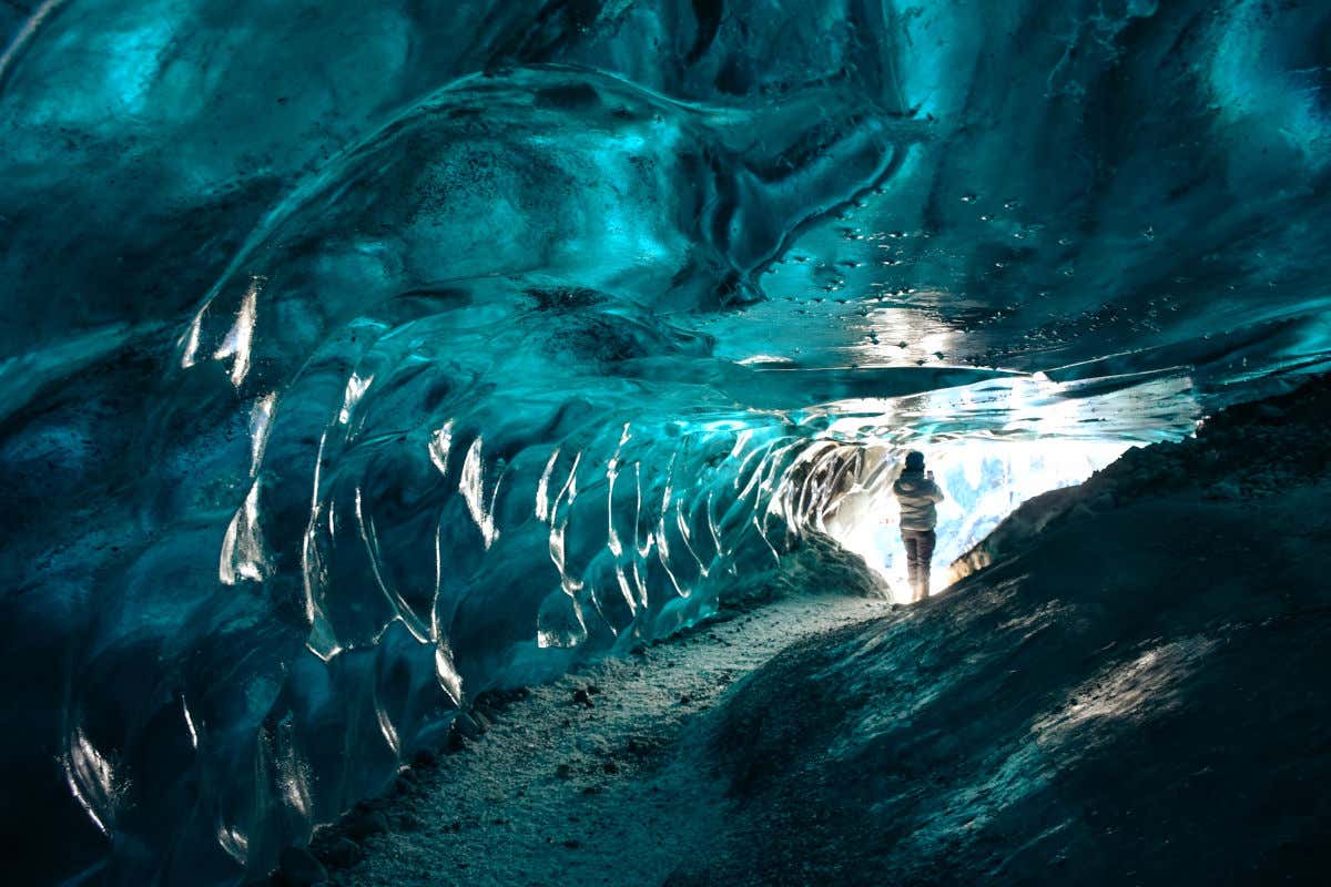 Una mujer de espaldas a la cámara siguiendo un estrecho sendero en el interior de una cueva cuyas paredes son totalmente de hielo