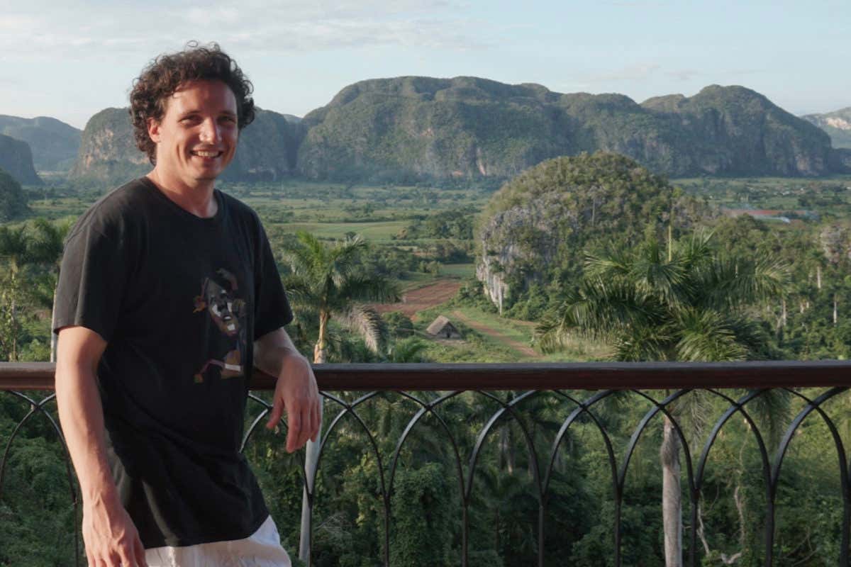 Un hombre asomado a un balcón, con unos paisajes de montaña de fondo