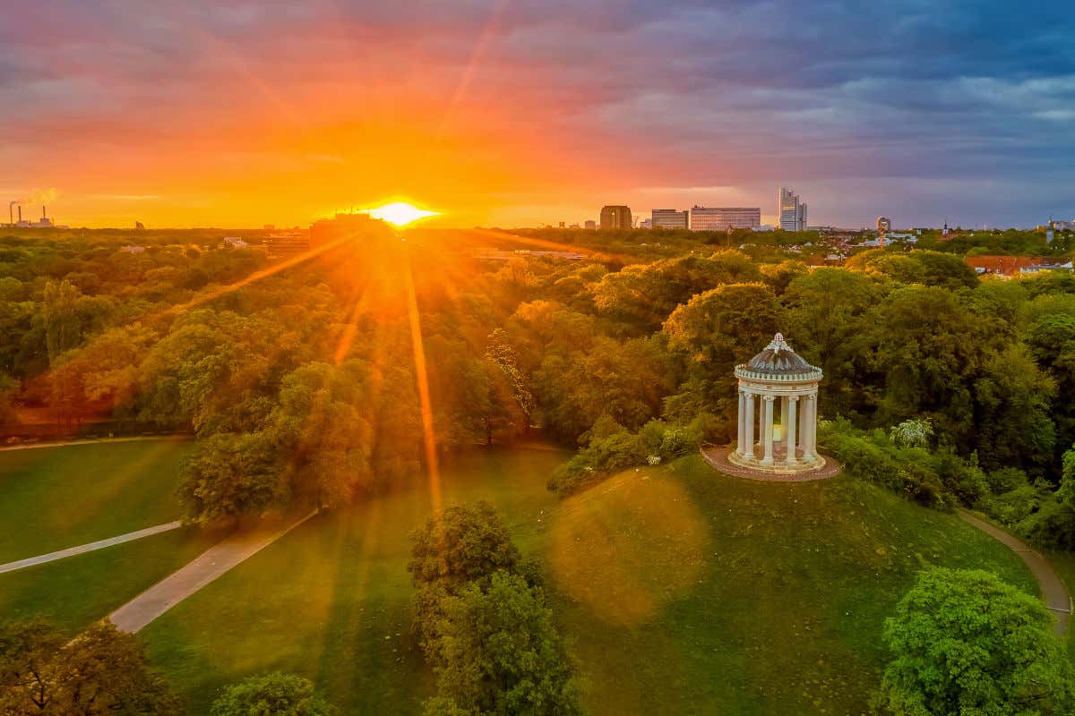 Vista aérea de un extenso bosque al atardecer con una pequeña colina coronada por un pequeño templete de estilo griego