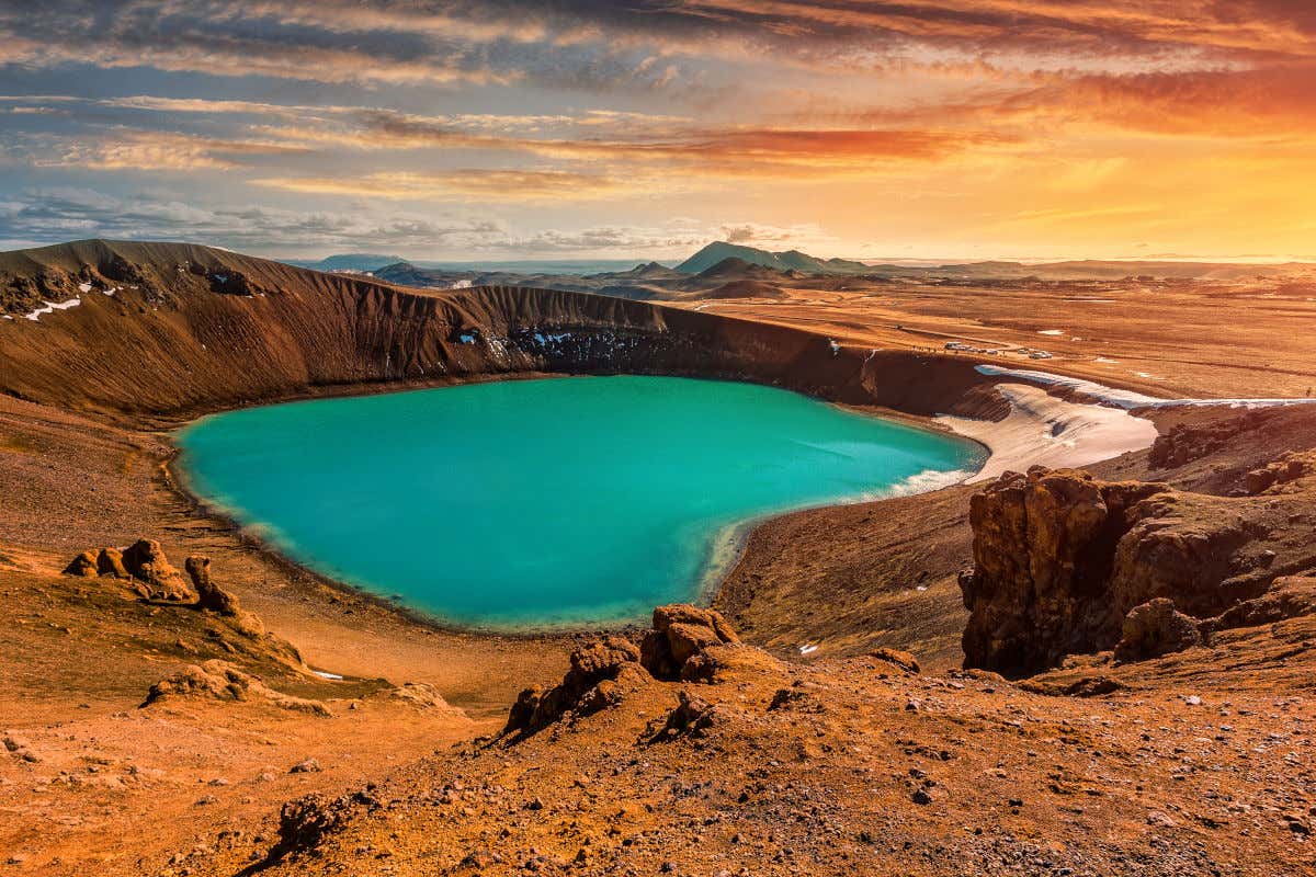 Un lago de aguas azules en el interior de un cráter volcánico rodeado por extensas llanuras y algunos otros conos volcánicos