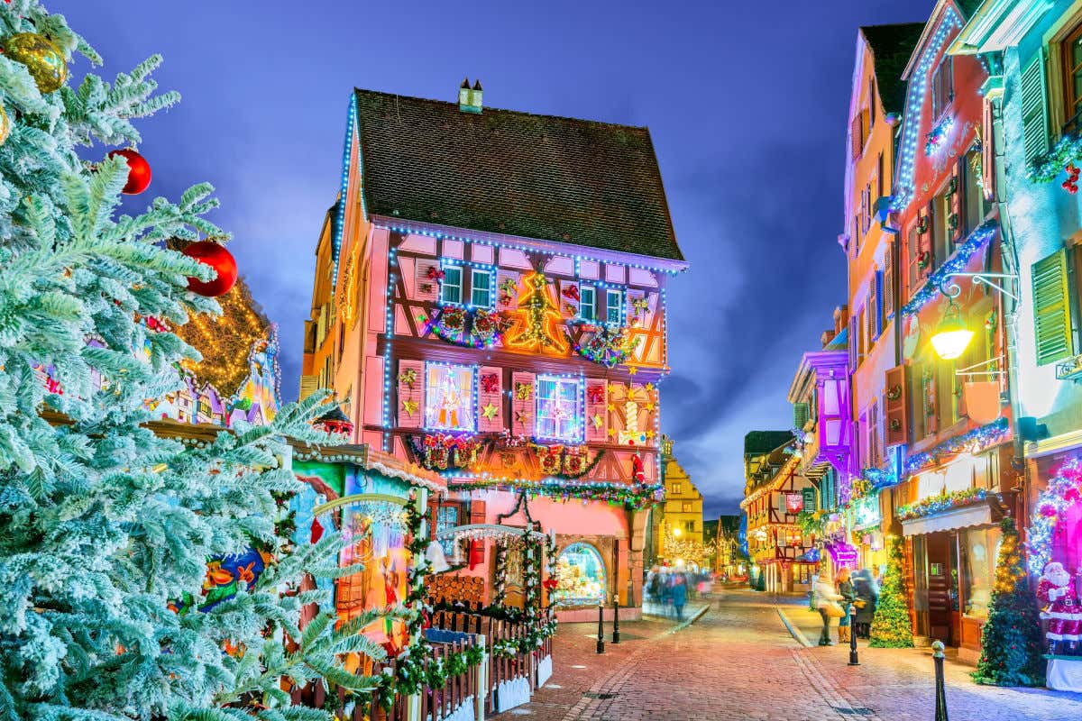 Una calle empedrada vista por la noche y decorada con un gran árbol de Navidad y diferentes luces y decoraciones en las fachadas de las casas