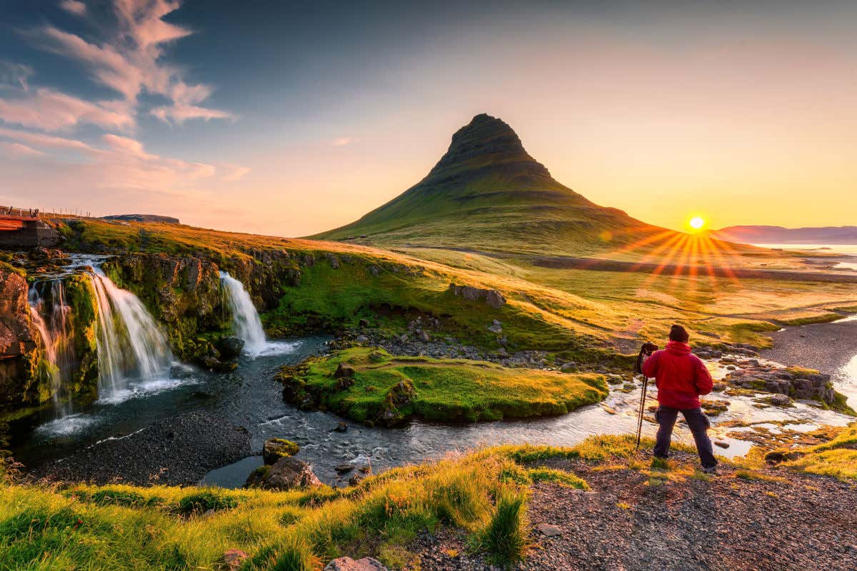 Un fotógrafo con cámara y trípode tomando imágenes de una colina al atardecer y un conjunto de pequeñas cascadas de Islandia