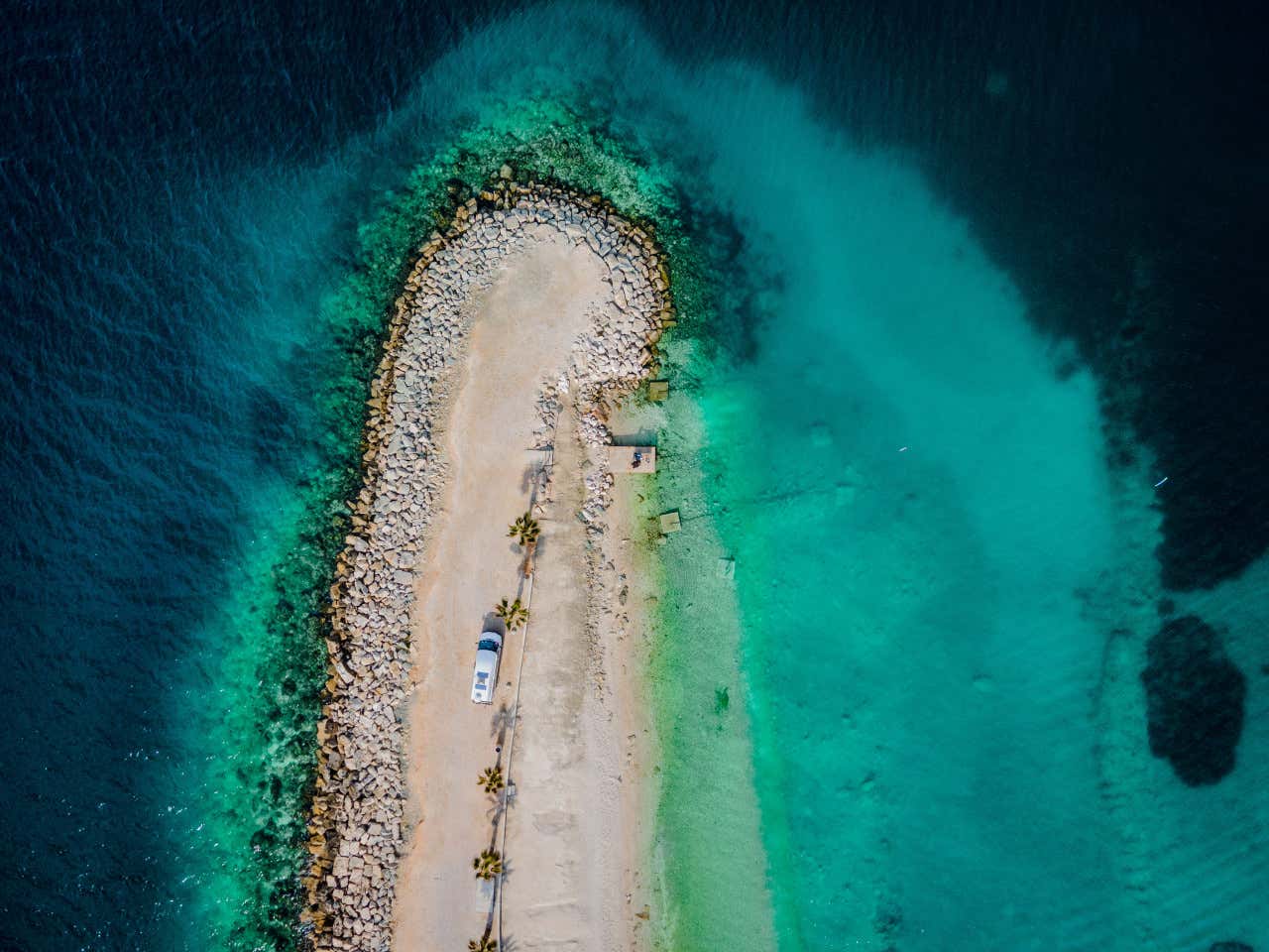 Vista aérea de la playa Kašjuni, con un camino de arena que divide el mar, hecha desde arriba con vista de dron