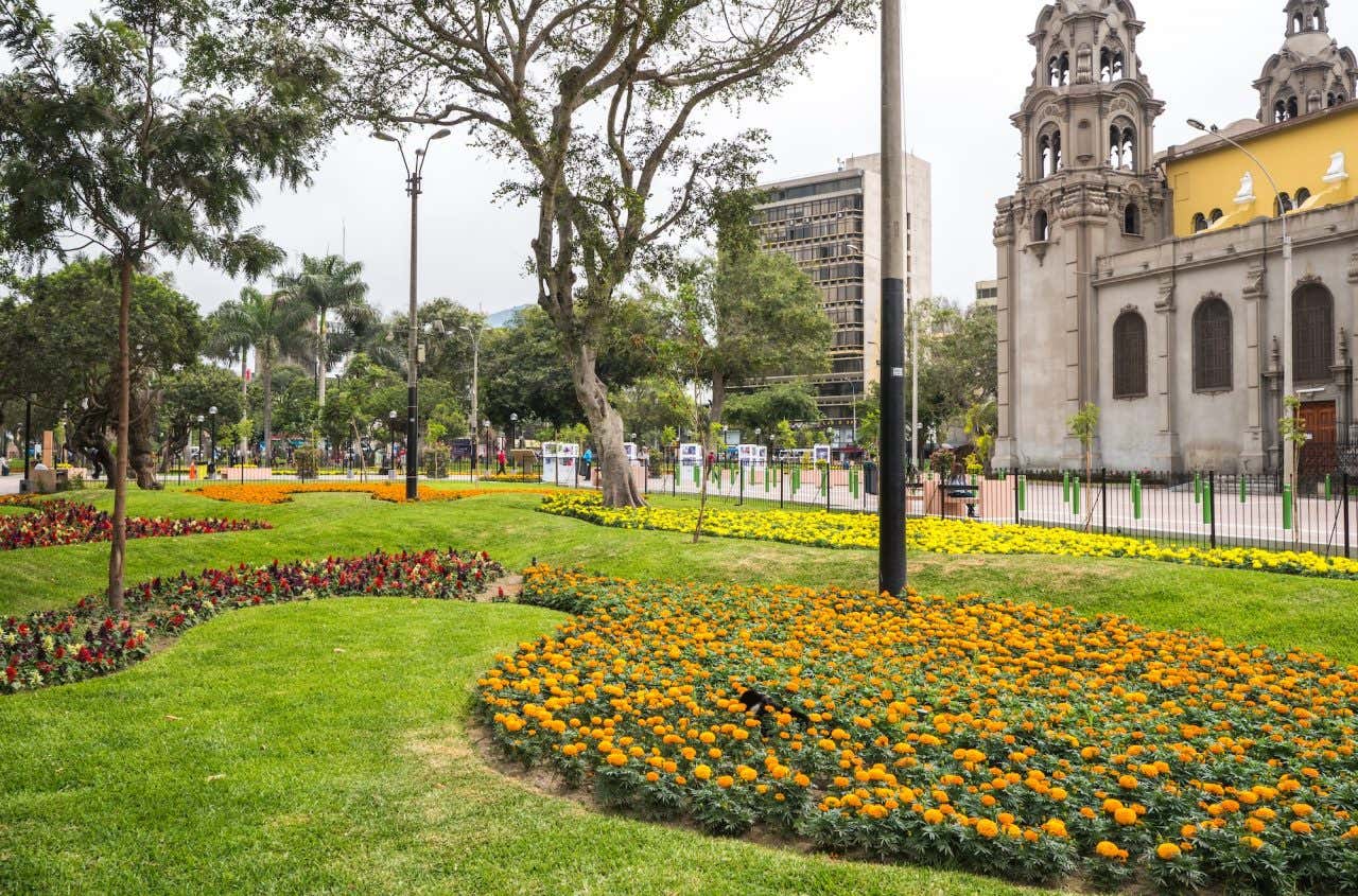 Jardim florido repleto de árvores e com uma igreja ao lado