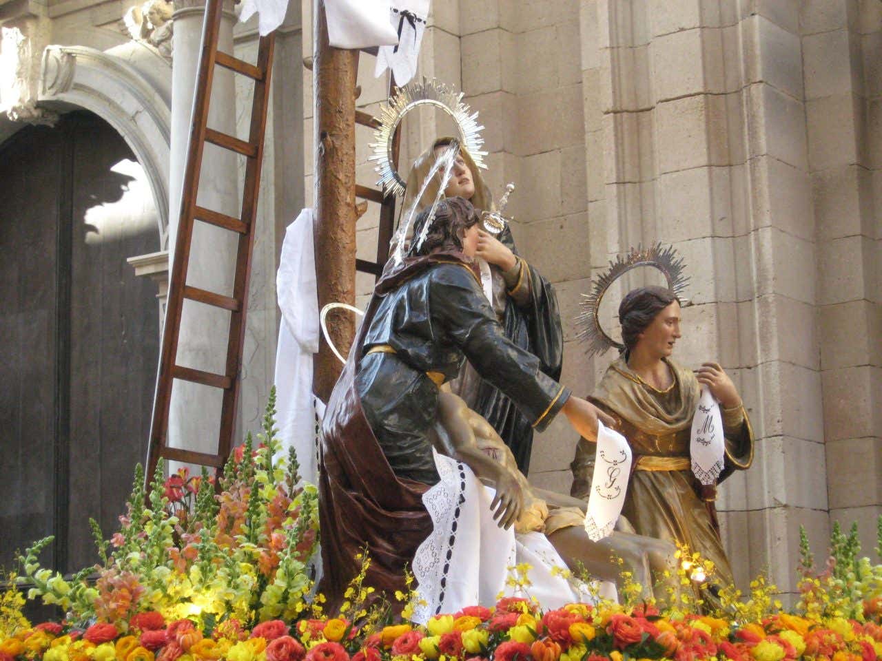 Statue in legno dipinto che rappresentano la deposizione del corpo di Cristo dalla croce, con la madonna piangente. La composizione scultorea è posizionata su una pedana decorata con fiori gialli e arancioni