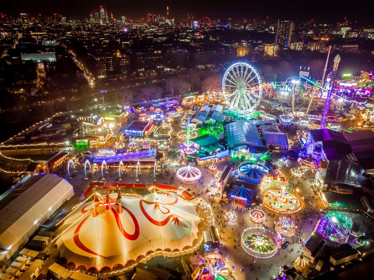 Veduta notturna dall’alto di Winter Wonderland a Hyde Park, Londra, con ruota panoramica, giostre illuminate e stand natalizi