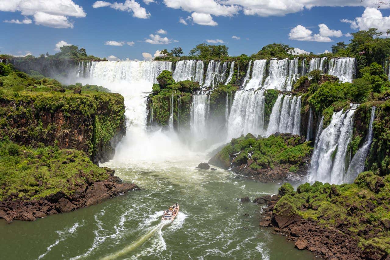 Iguazú falls seen from the Argentinian side with a boat sailing at the bottom of the shot.