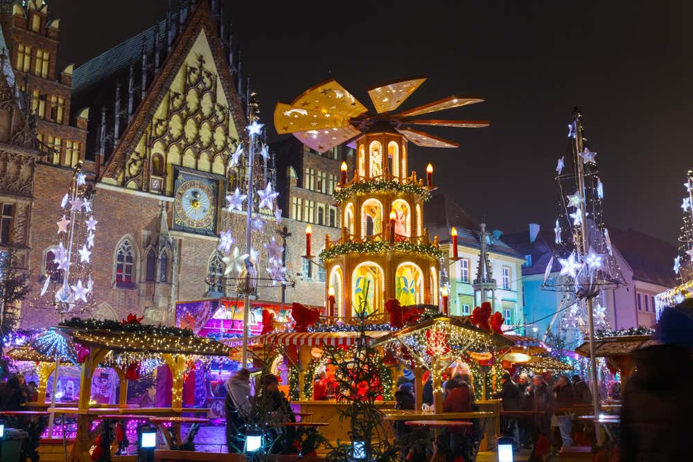 Il mercatino di Natale di Breslavia di notte nella piazza del Municipio, con una grande piramide natalizia in legno illuminata al centro, circondata da bancarelle decorate, alberi di luce e decorazioni a forma di stelle luminose