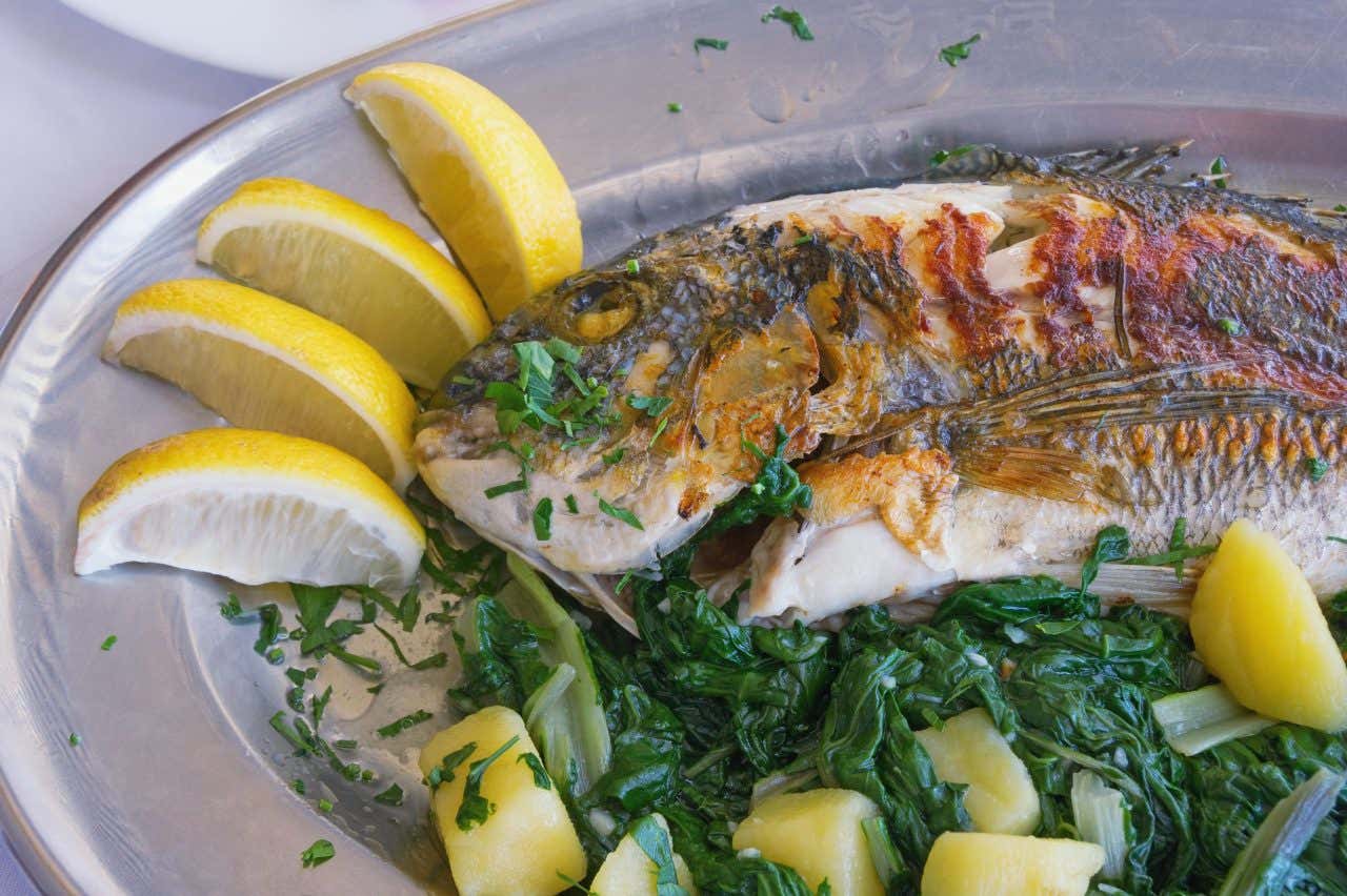 Overhead view of a freshly grilled fish on a bed of steamed spinach and lemon wedges place along the edge of the plate