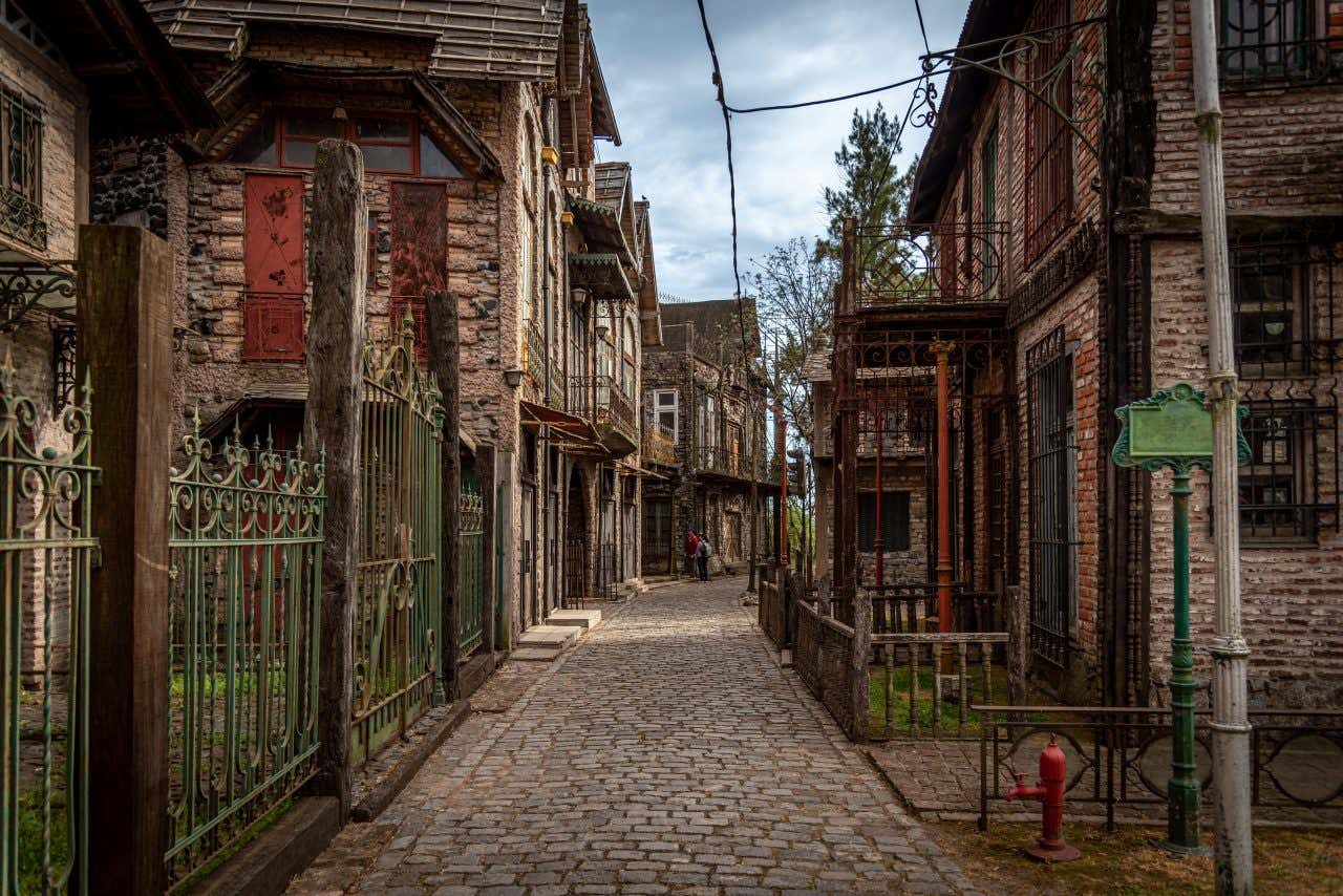 A narrow cobbled street with fantasy medieval houses on either side and some people in the distance.