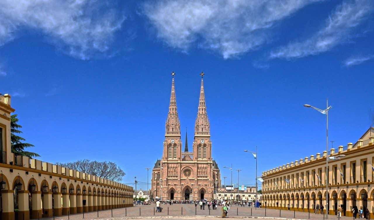 The Basilica of Luján as seen from afar, with people walking on the street level and a mostly clear blue sky in the background.