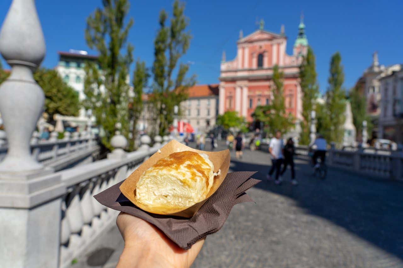 A hand holds out a Štruklji on a black napkin in Ljubljana, Slovenia on a clear sunny day