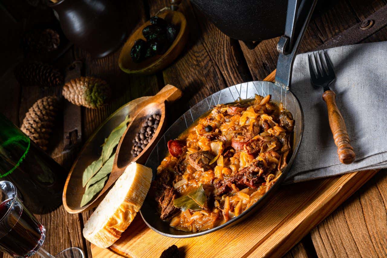 Piatto tipico polacco con carne, cipolla e verdura, servito con pane e grani di pepe su una tavola con alloro e pigne