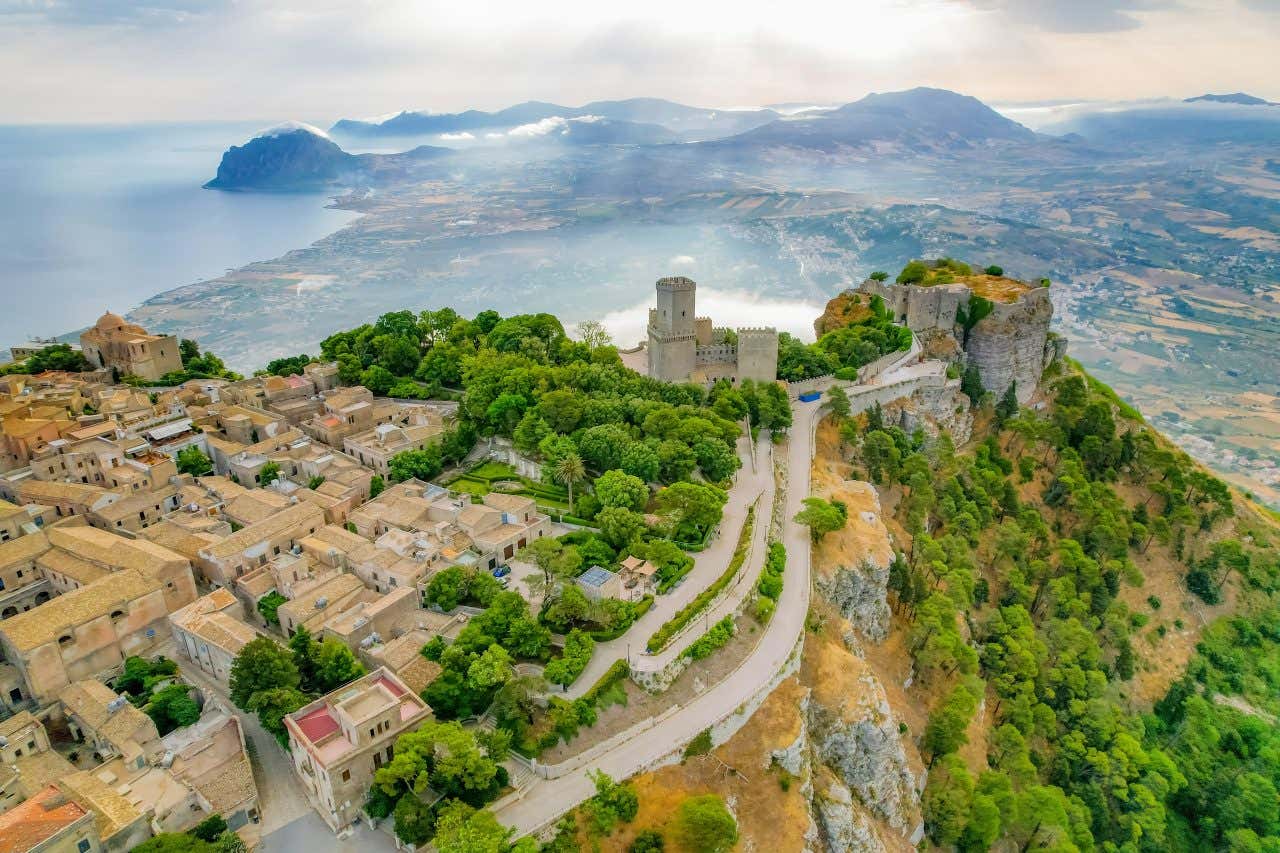 Il centro storico di Erice, con le rovine di un antico castello, fotografato dall'alto, mentre nella vallata sottostante si intravedono verdi colline e il mare