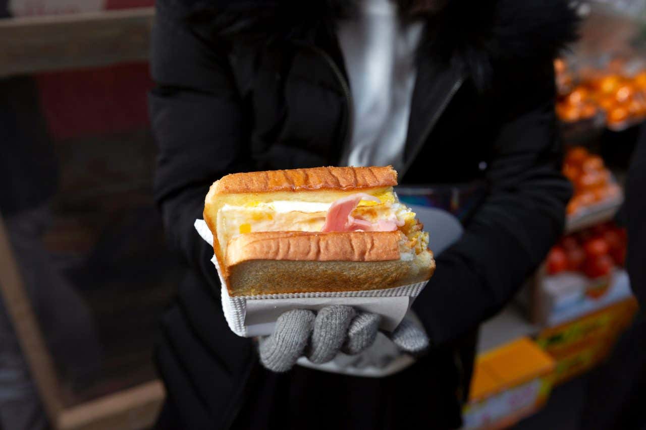 A pair of gloved hands hold a gilgeori-ppang sandwich in Seoul, South Korea, a secret foodie destination
