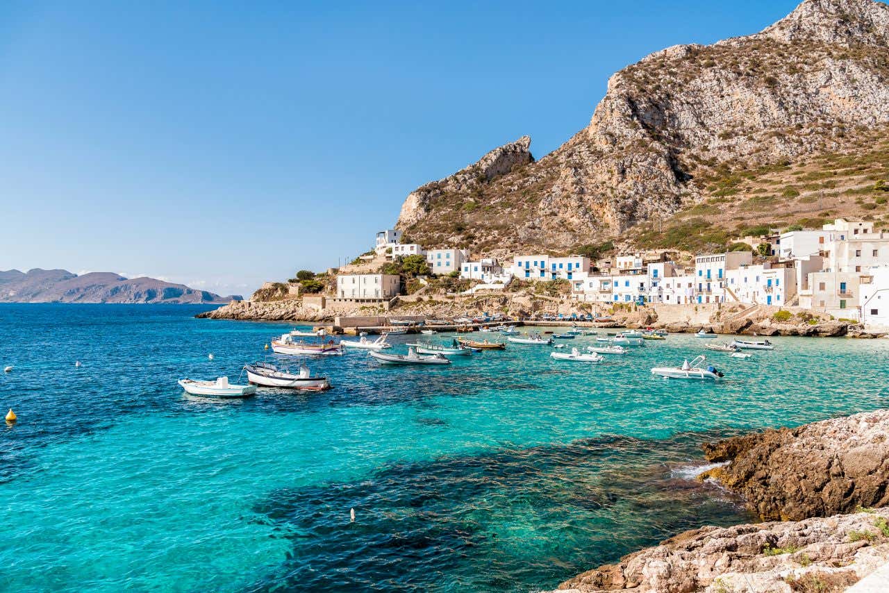 Un piccolo borgo peschereccio di casette bianche arroccate su una scogliera davanti a un mare turchese con alcune piccole imbarcazioni che galleggiano sull'acqua
