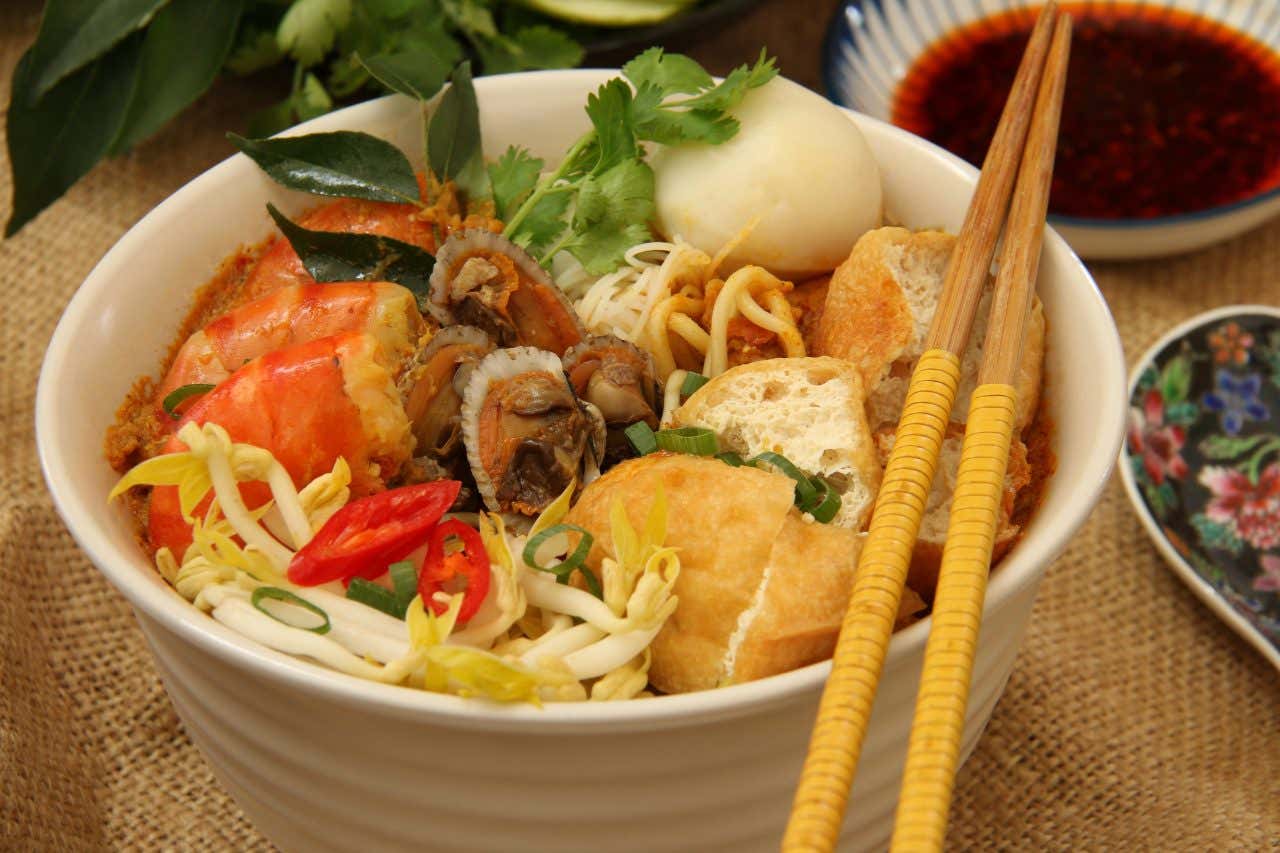 A bowl of curry laksa with all the trimmings, and a pair of chopsticks set on top of the bowl